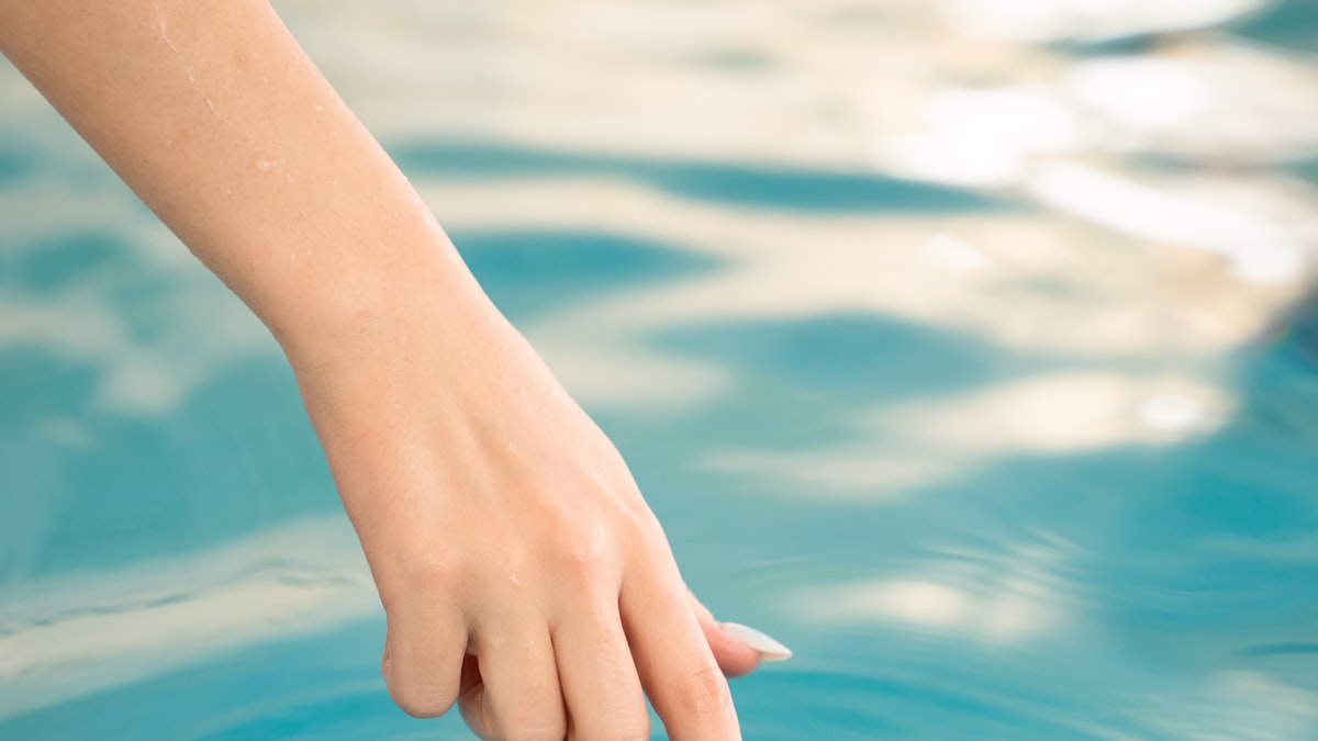 Mão tocando a superfície da água azul de uma piscina